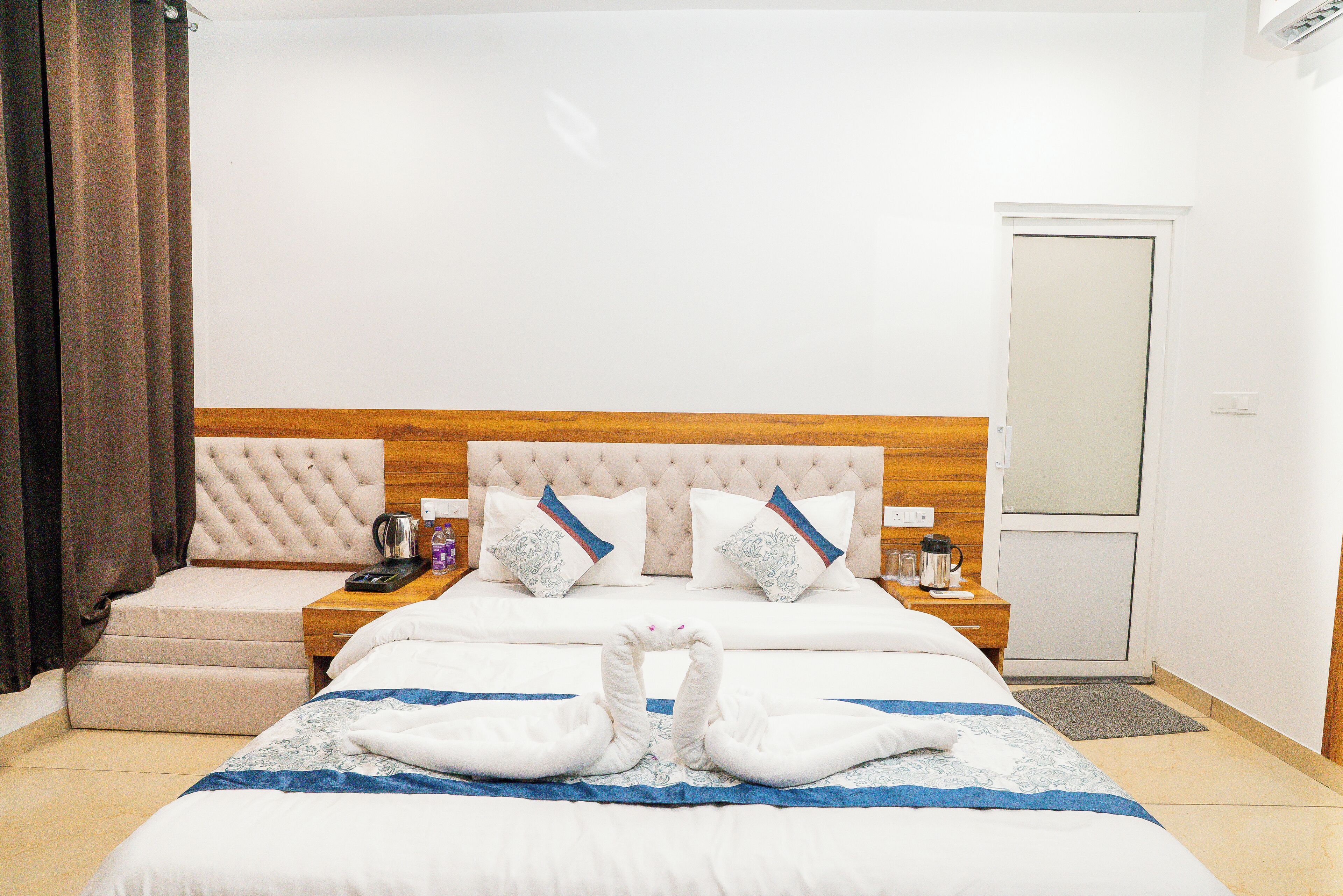 Una habitación de hotel con una cama grande, un cabecero de madera, dos mesitas de noche con lámparas y una puerta.