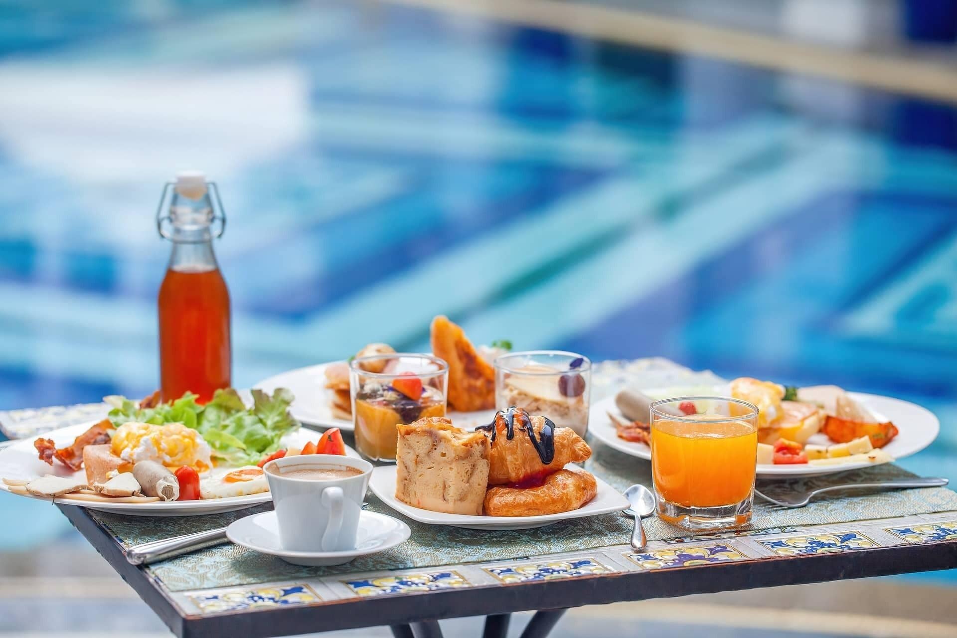 Un bufé de desayuno con diversos platos, una botella de jugo y una taza de café sobre una mesa junto a una piscina.
