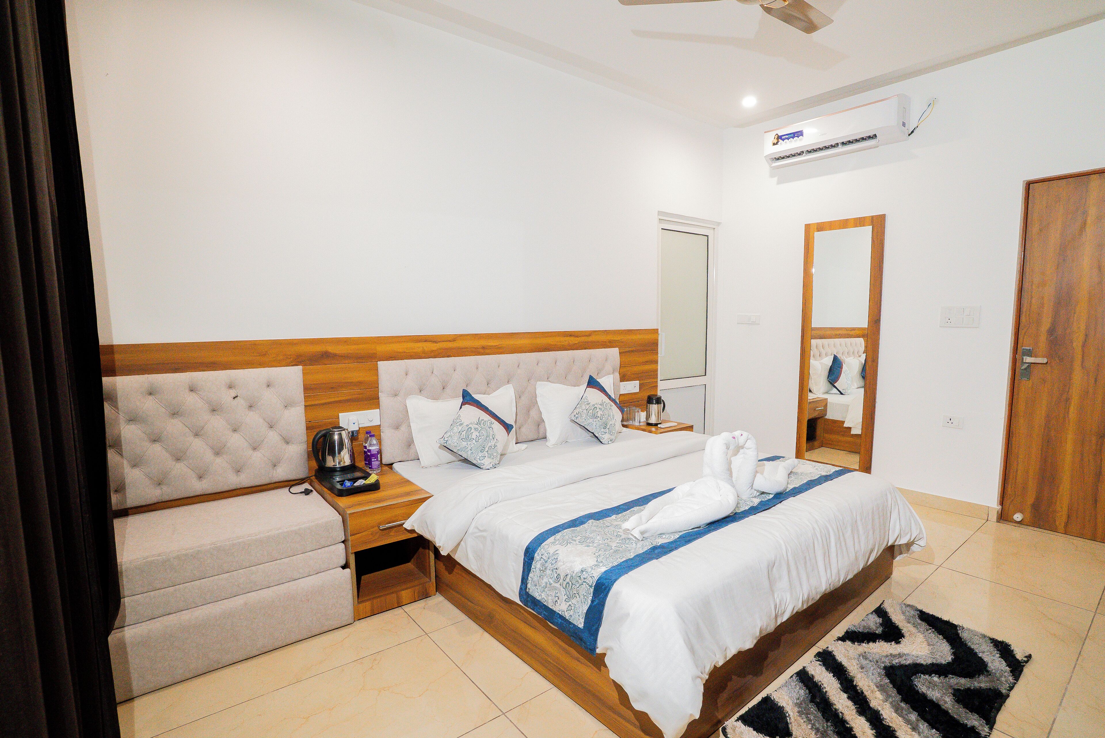 Una habitación de hotel con una cama, una mesita de noche, una silla, un espejo y un equipo de aire acondicionado.