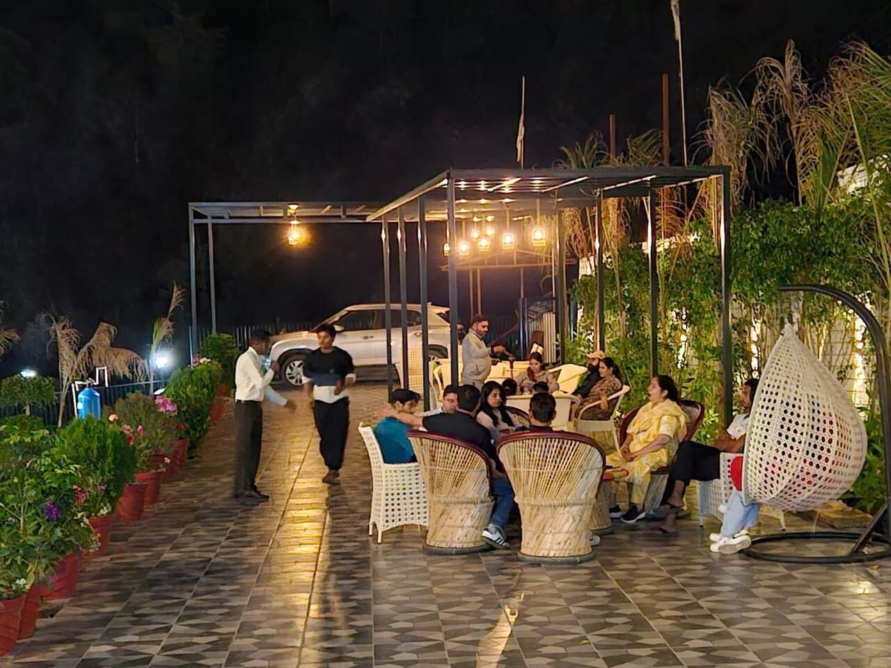 Un espace extérieur aménagé avec des chaises en osier et une partie abritée, le tout entouré de plantes en pot.
