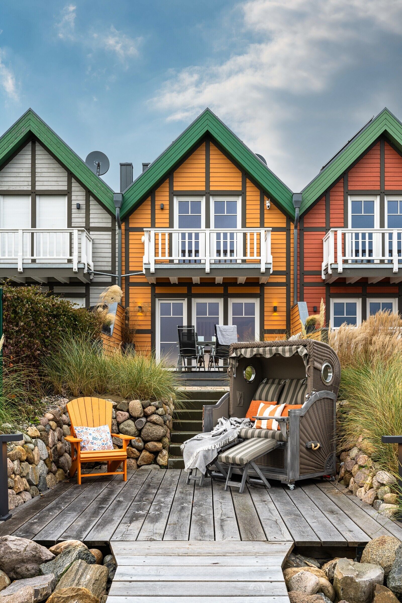 A multi-story building with balconies, a deck with outdoor furniture, and a large window.