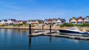 A row of colorful houses by a calm waterfront with a dock and a boat. - Family-friendly vacation home "Hafenspaß" with water view, close to the beach (Olpenitz)