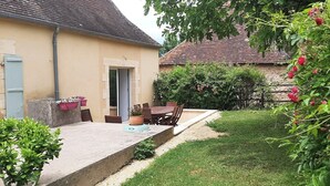 A patio with a table and chairs, a small garden area with bushes and flowers, and a building with a tiled roof and beige walls. - Country house in the heart of Périgord Noir in Rouffignac  (Rouffignac-Saint-Cernin-de-Reilhac)