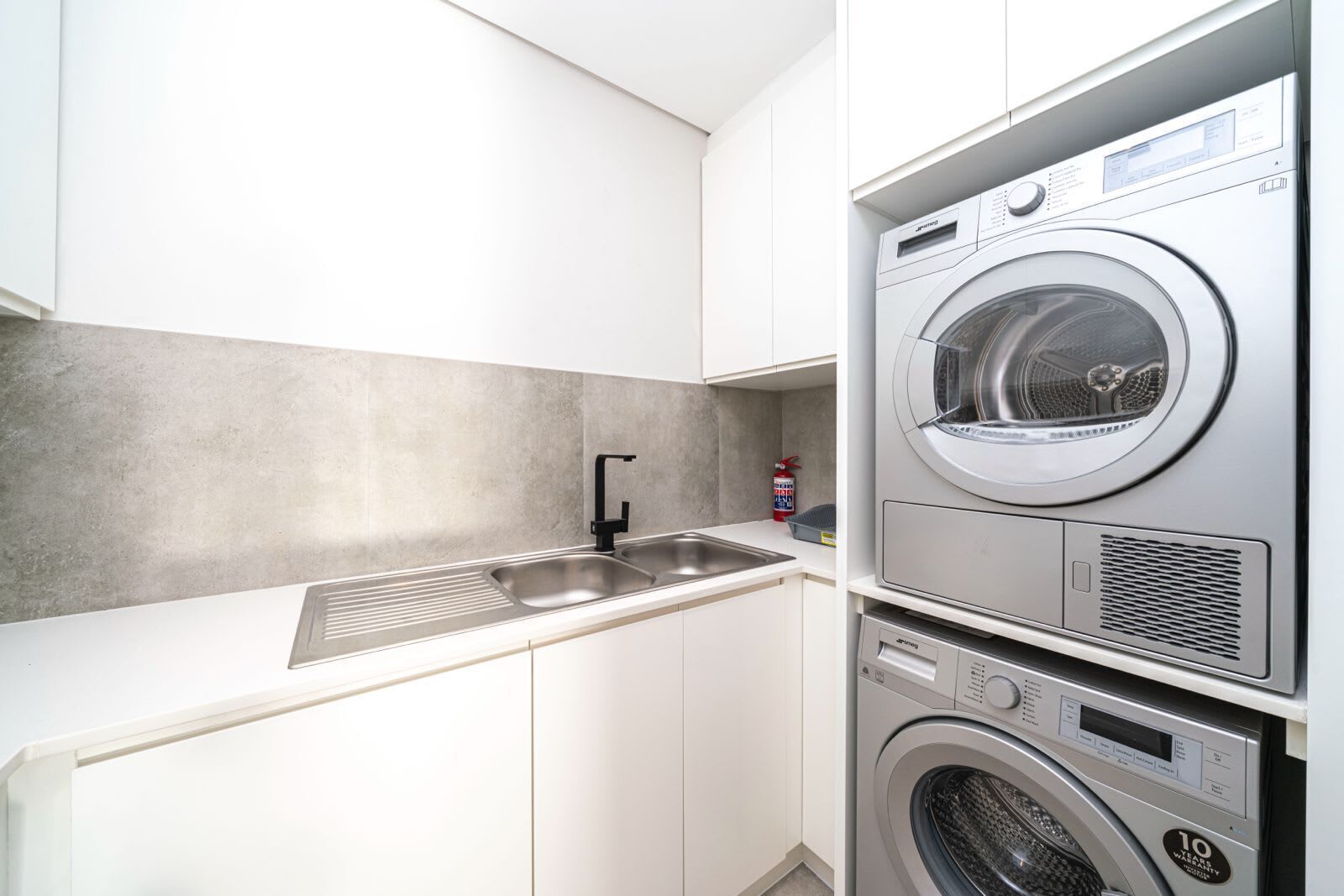 A compact laundry room with a built-in washer and dryer, a stainless steel sink, and a grey backsplash.