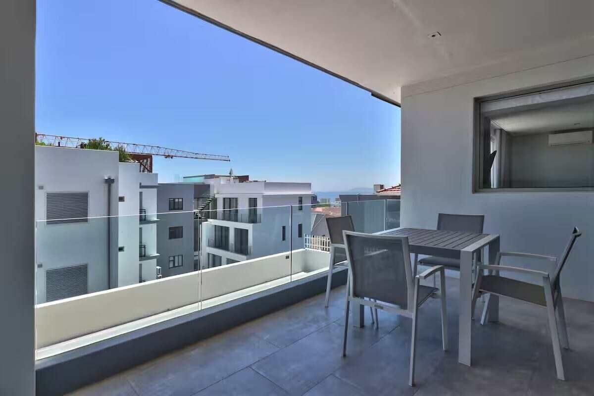 A balcony with a table and chairs, overlooking a residential area with modern buildings.
