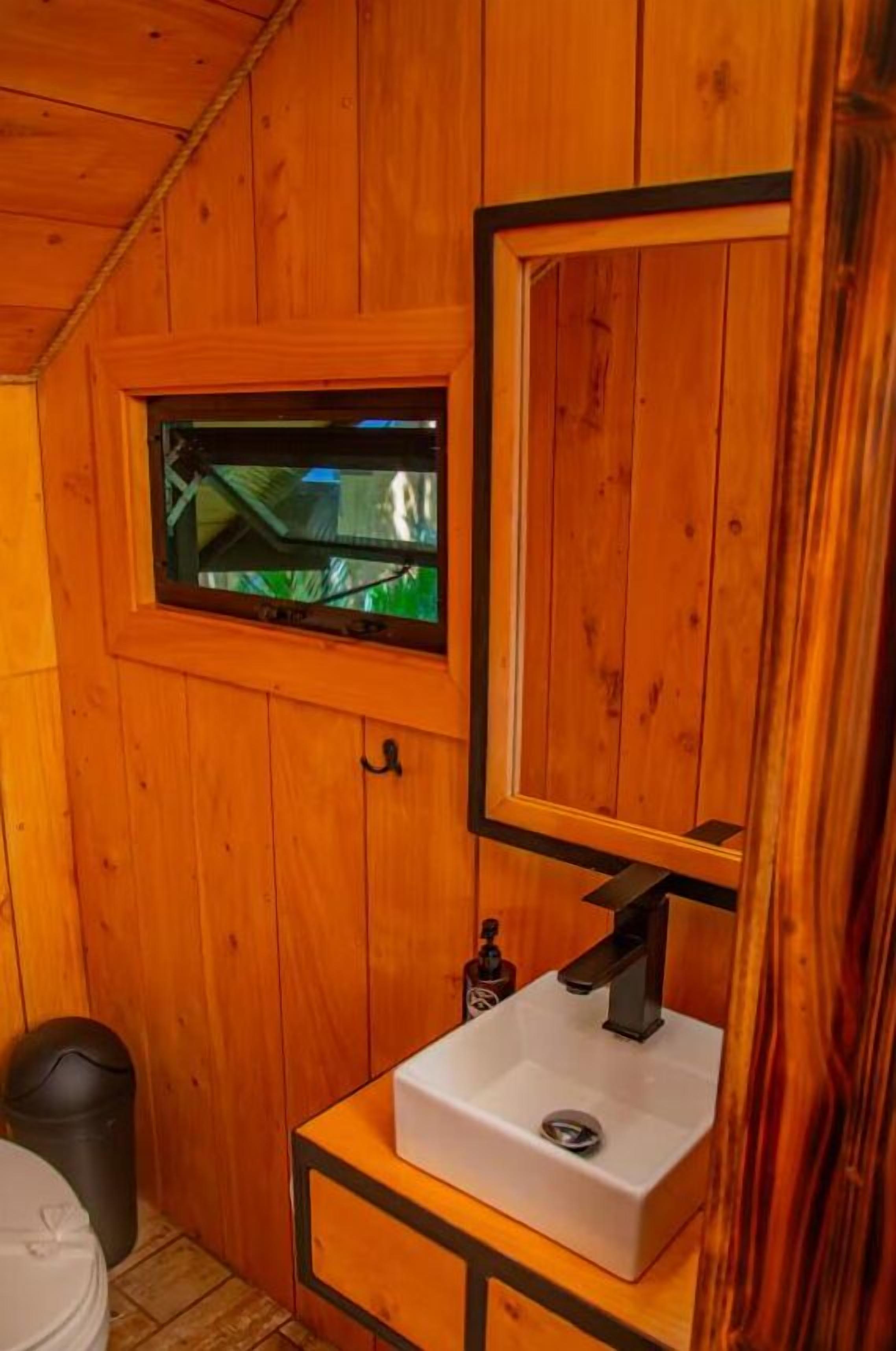 A wooden cabin bathroom with a white sink, a window, and a mirror.