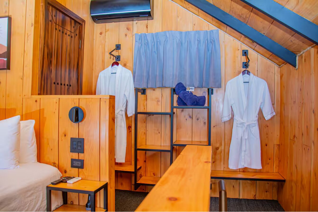 Een houten hutje met een bed, een tafel en twee paspoppen in badjassen.