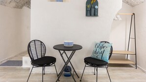 Una habitació petita amb dues cadires de filferro negres, una taula rodona amb un bol blau, una prestatgeria penjada amb plantes en testos i un moble prestatgeria vertical.