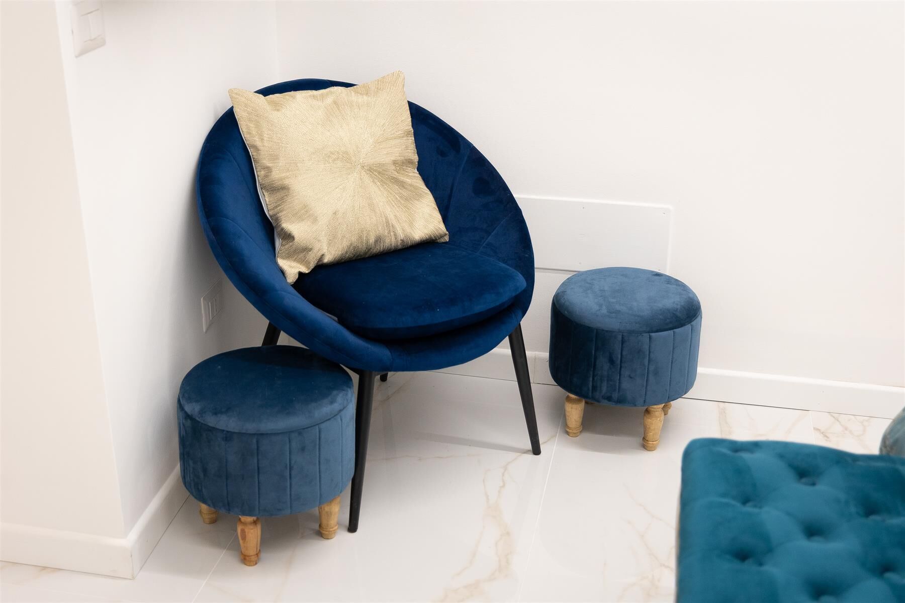 Ein blauer Sessel mit Kissen, zwei passende Hocker und ein gepolsterter Hocker.