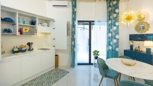 Una cuina moderna amb armaris blancs, una zona de menjador amb taula de marbre blanc, cadires color turquesa i una làmpada decorativa al sostre.