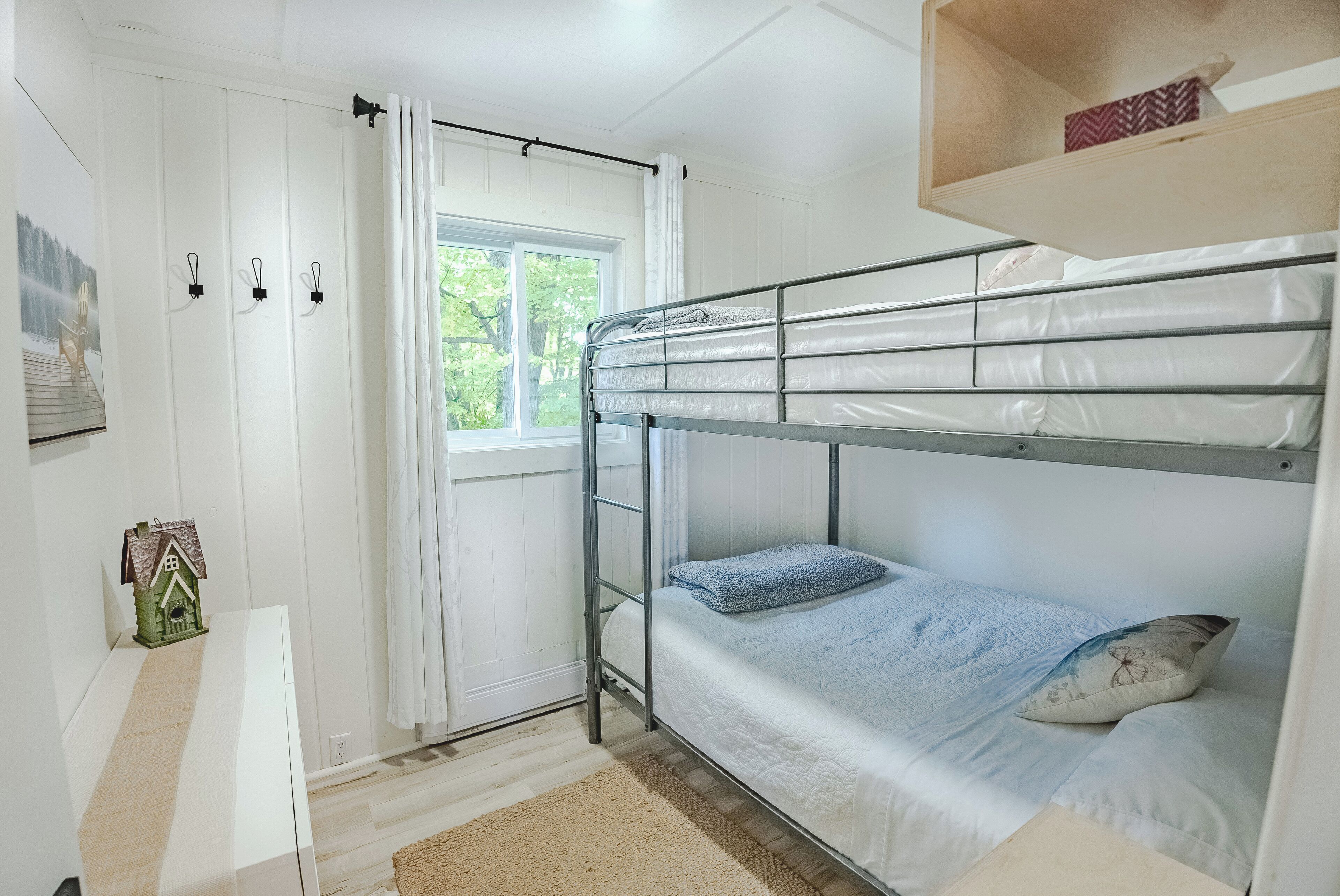 A bunk bed room with a window, a small shelf, and a decorative house model.