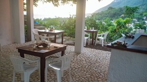 An outdoor patio with stone flooring, white plastic chairs, and tables set for dining.