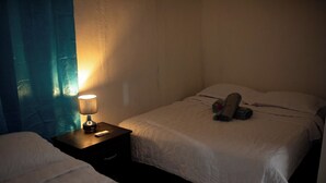 A hotel room with two beds, a nightstand with a lamp, and a blue curtain.