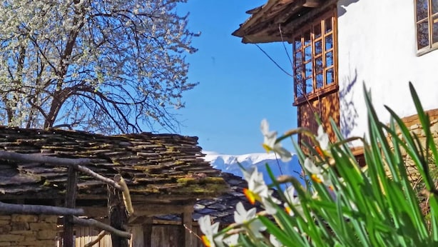 Un edificio rústico con pared de piedra y vigas de madera, cerca de madera y cielo azul despejado.