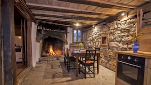 Comedor con suelo de piedra, chimenea, vigas de madera y pared de piedra.