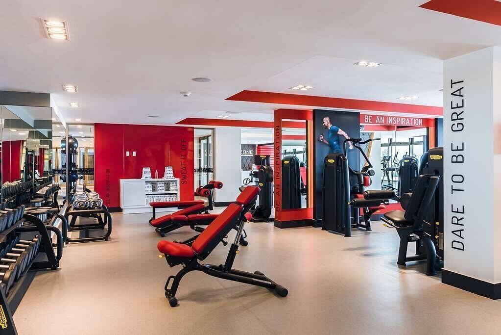 A gym with red and white walls, various exercise equipment, and motivational posters.