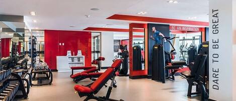 A gym with red and white walls, various exercise equipment, and motivational posters.