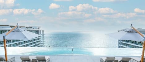 A poolside area with lounge chairs and umbrellas, overlooking a calm sea.