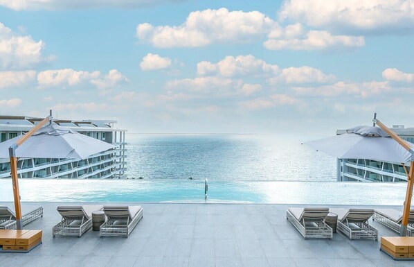 A poolside area with lounge chairs and umbrellas, overlooking a calm sea.
