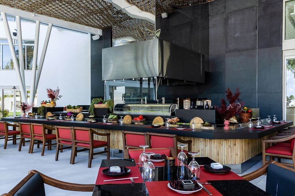 A modern outdoor bar area with a long counter, red chairs, and a large screen.