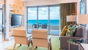 Una habitación de hotel con balcón, televisión de pantalla plana, dos sillones, un sofá y una mesa de comedor.