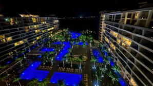 Un resort con varias piscinas, palmeras y senderos iluminados por la noche.