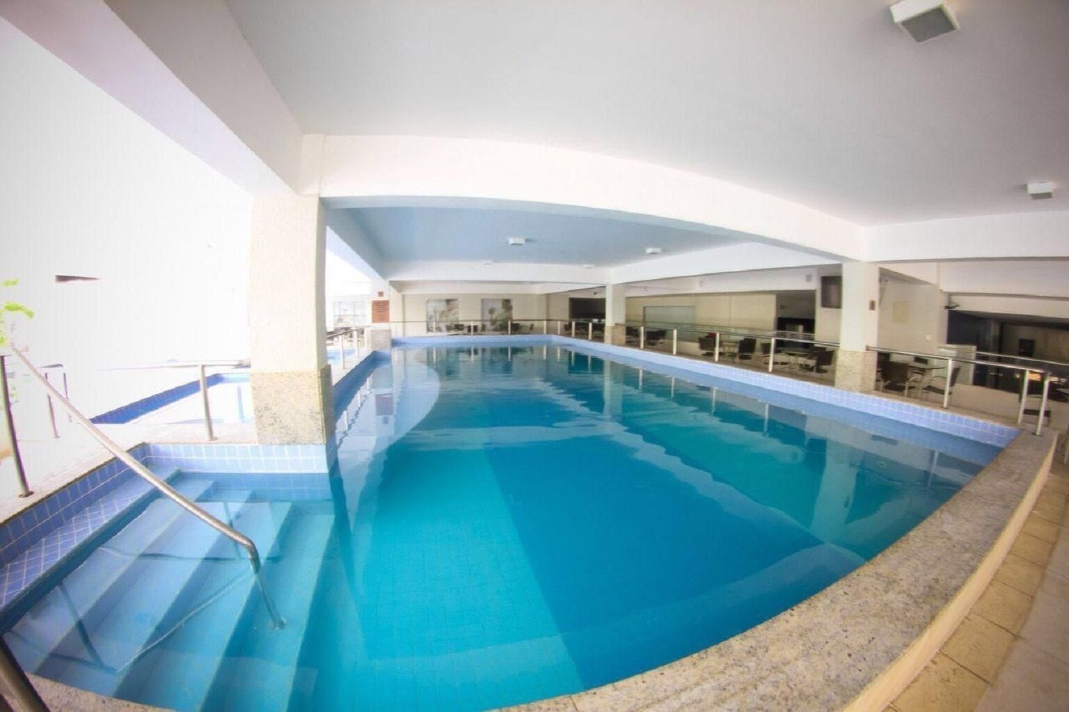 An indoor swimming pool with clear blue water, a glass railing, and a tiled floor.
