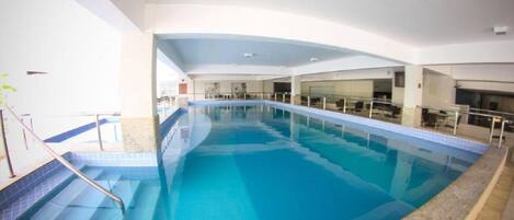 An indoor swimming pool with clear blue water, a glass railing, and a tiled floor.