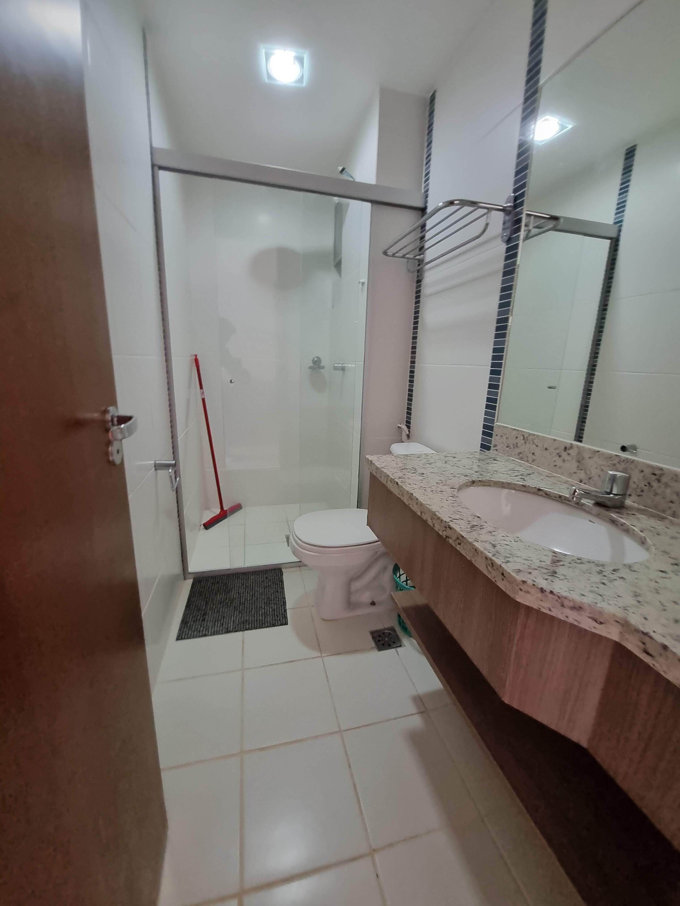 Une salle de bain équipée de toilettes, d’un lavabo, d’un miroir, d’une douche et d’une serpillière appuyée contre le mur.