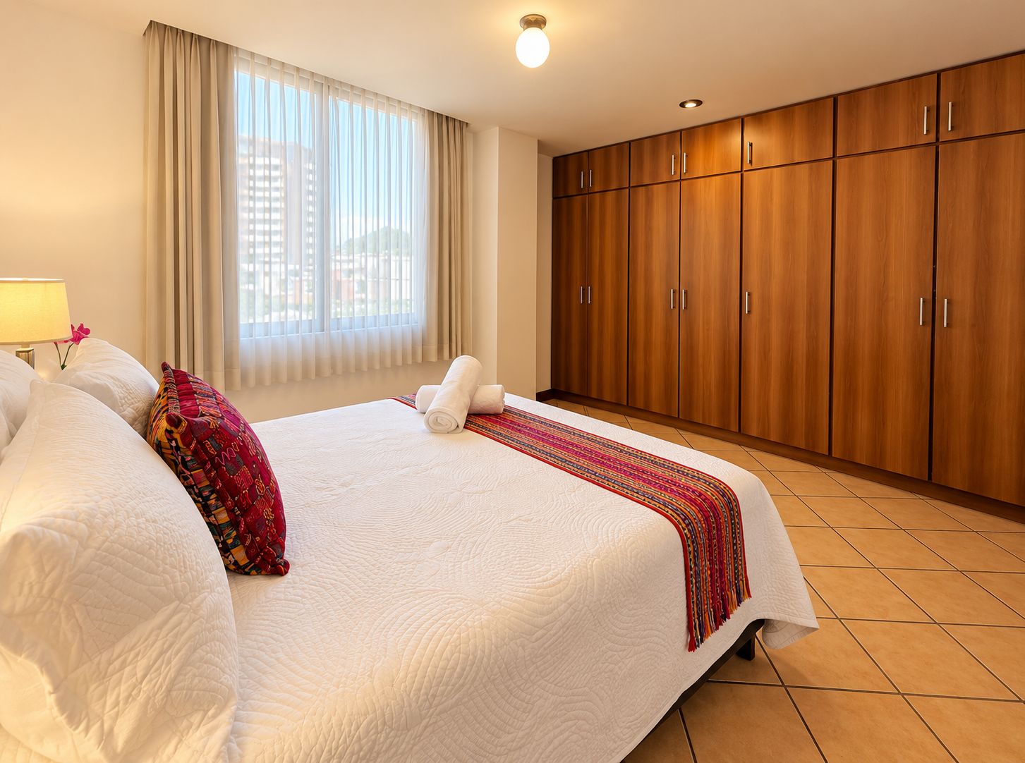 Una habitación de hotel con una cama grande, un armario y un ventanal con cortinas.