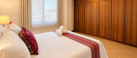 Una habitación de hotel con una cama grande, un armario y un ventanal con cortinas.