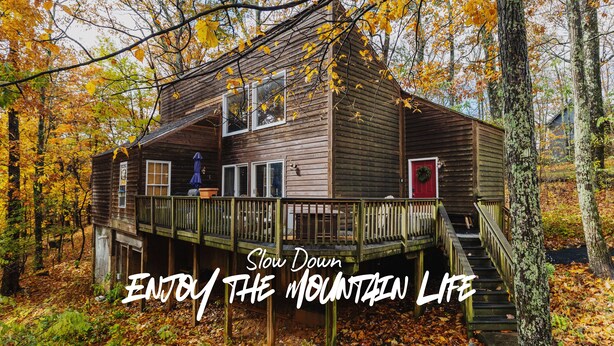 A wooden cabin with a deck, surrounded by autumn foliage.