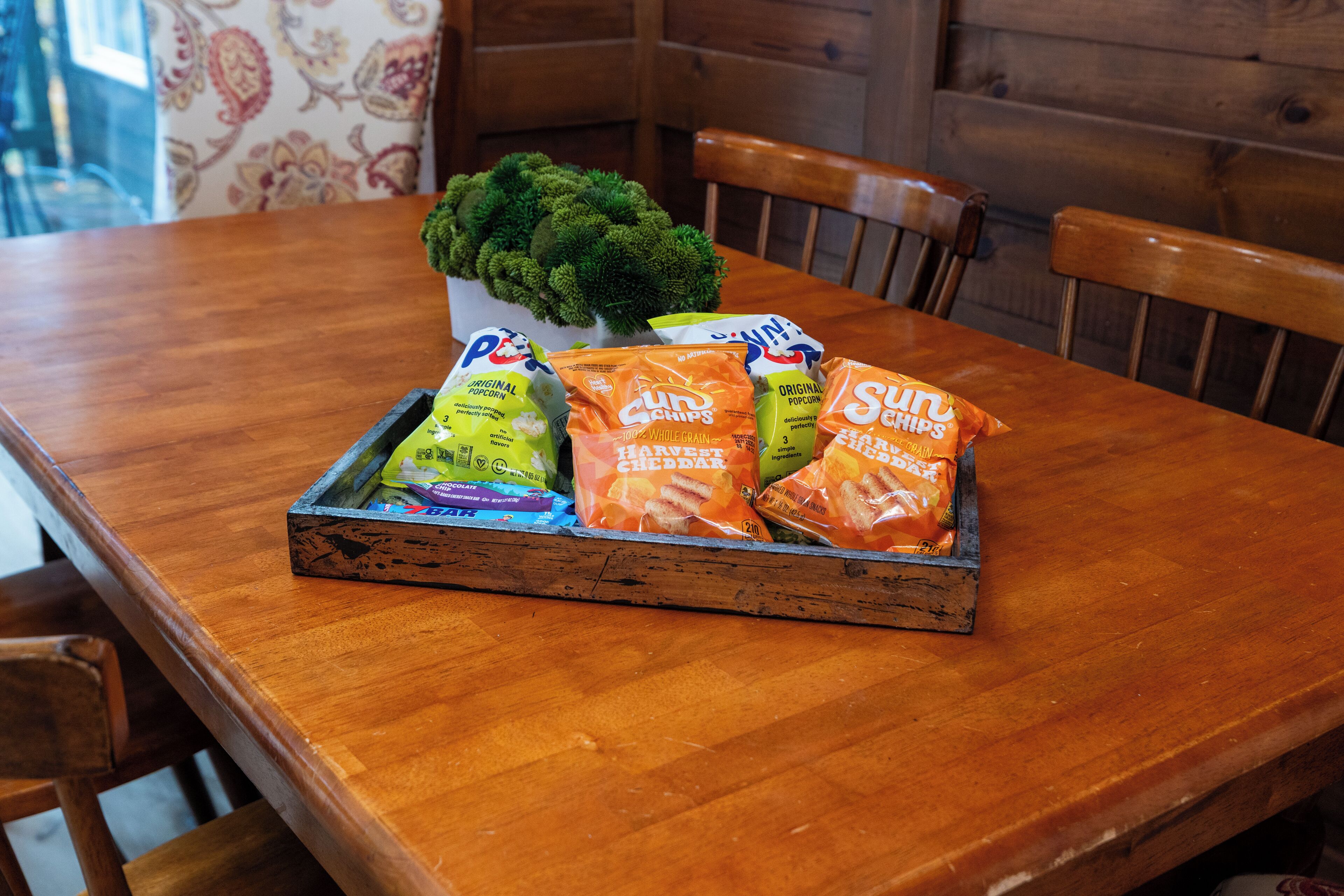 Una mesa de madera con un recipiente que contiene bolsas de palomitas y una planta en maceta.