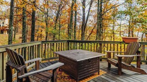 A wooden deck with a table and two chairs, surrounded by a railing and autumn foliage.