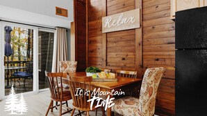 A dining area with wooden walls, a sign that says "Relax Unwind & ENJOY", and a view of trees outside.