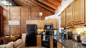A cozy kitchen with wooden cabinets, a black refrigerator, a microwave, and a coffee bar.