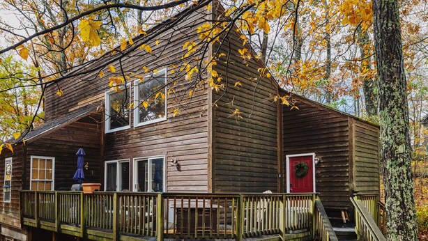 Eine Holzhütte mit einer Terrasse, umgeben von Herbstlaub.