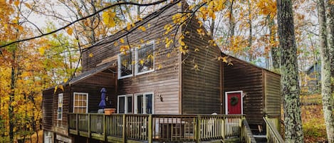 A wooden cabin with a deck, surrounded by autumn foliage.