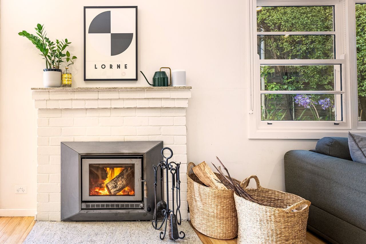A fireplace with a modern design, a framed picture above it, and a window with a view of greenery.