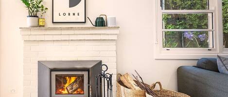A fireplace with a modern design, a framed picture above it, and a window with a view of greenery.