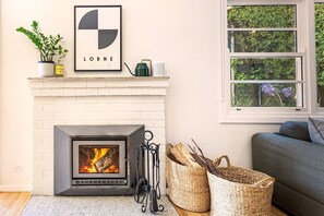 Une cheminée au design moderne, un tableau encadré au-dessus, et une fenêtre donnant sur un paysage verdoyant.