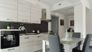 Een moderne keuken met lichte houten kastjes, een roestvrijstalen afzuigkap, en een eethoek met een tafel en stoelen.
