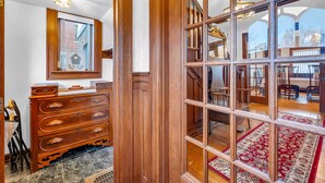 Un intérieur en bois agrémenté d’un grand miroir, d’une commode en bois et d’une vue sur un coin repas, visible à travers une porte vitrée.