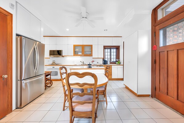Una cocina moderna con armarios blancos, un refrigerador de acero inoxidable, una mesa de comedor de madera con sillas y un ventanal grande.
