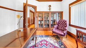 Une pièce comprenant un bureau en bois, un fauteuil en cuir violet, un tapis à motifs et une vitrine contenant des objets décoratifs.