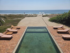 Un espace piscine avec des chaises longues et vue sur la plage.
