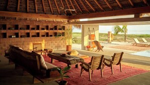 A spacious indoor area with a thatched roof, wooden furniture, and a view of the beach. - Mariana Uno · Luxury · Exclusive Bay Oaxaca (Puerto Escondido)