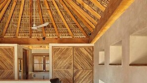 A bedroom with a high ceiling, wooden beams, a bed with a striped bedspread, a nightstand, and a wall with a geometric pattern. - Mariana Uno · Luxury · Exclusive Bay Oaxaca (Puerto Escondido)