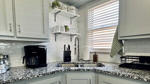 Eine Küche mit weißen Schränken, einer Granit Arbeitsplatte, einer Kaffeemaschine und einem Fenster mit Jalousien.