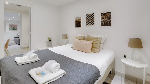 A modern hotel room with a neatly made bed, two bedside tables, and a small side table with a lamp. - Bluestay 301 - Superb apartment in Paris (Paris 02 Bourse)